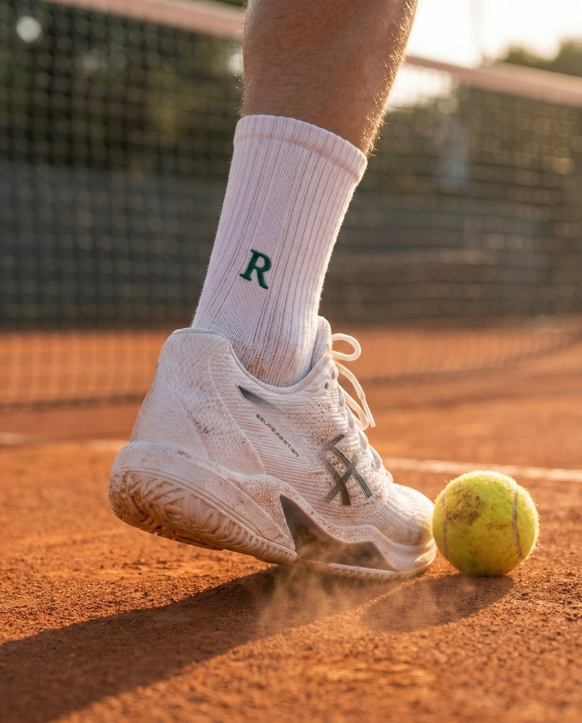 Che regalo fare a chi gioca a tennis: calze da tennis bianche con le iniziali ricamate in verde, accanto a una racchetta e a un tubo di palline