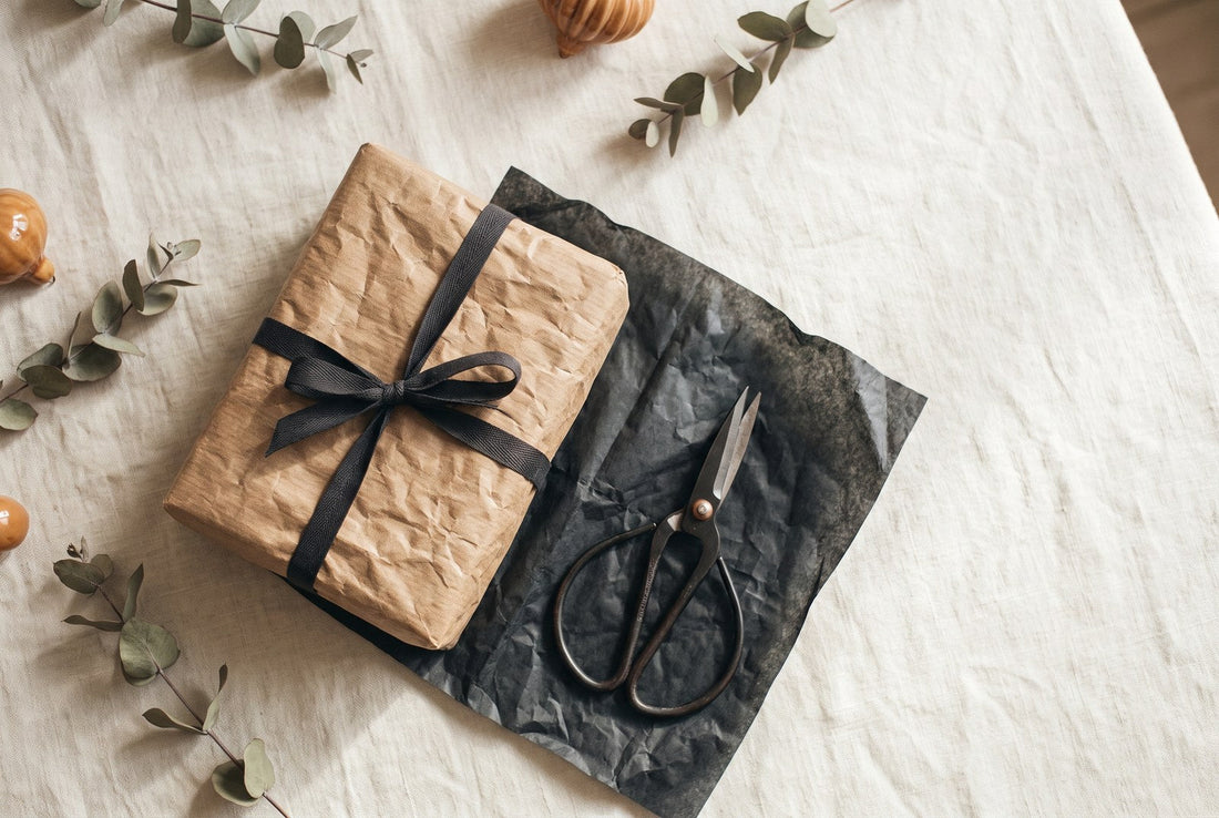 Regalo di Natale per chi ha già tutto: pacchetto avvolto in carta avorio e spago accanto a un ramo di abete