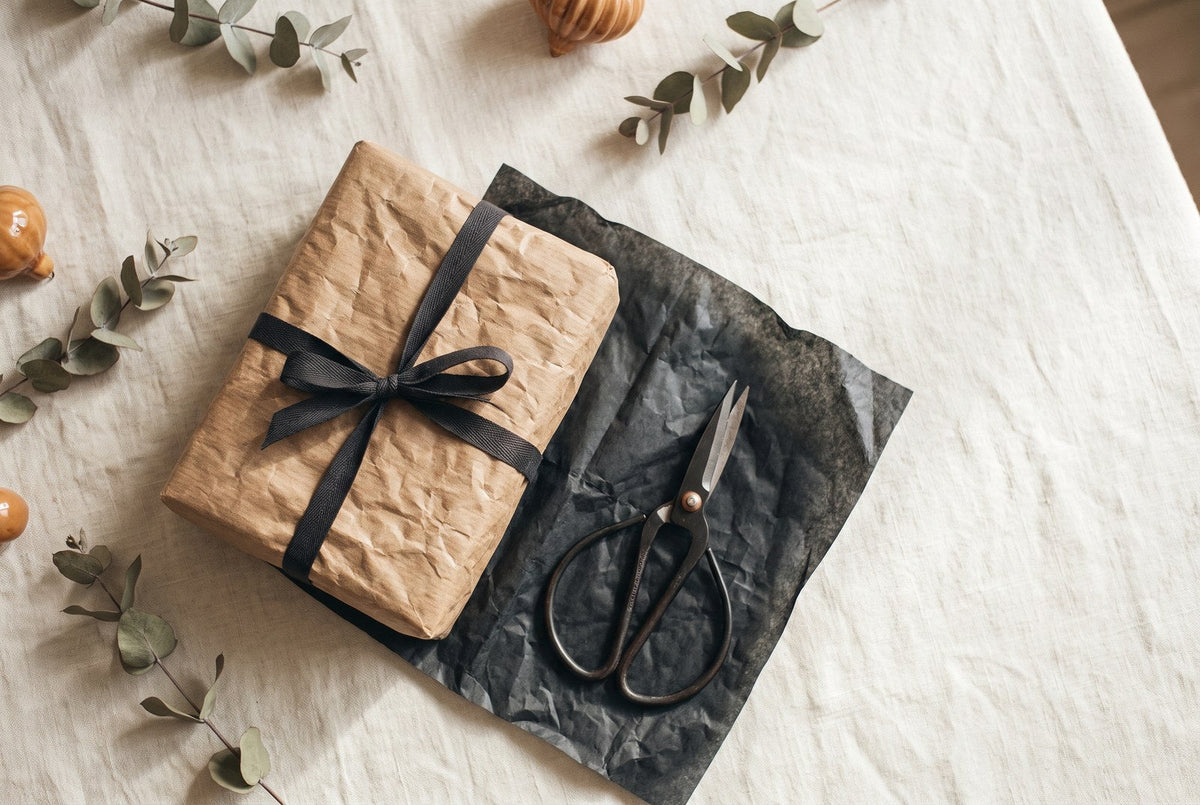 Regalo di Natale per chi ha già tutto: pacchetto avvolto in carta avorio e spago accanto a un ramo di abete