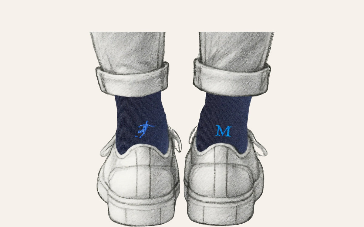 regalo per chi gioca a calcio: calze blu Individual Socks con il calciatore ricamato in blu royal su una calza e l'iniziale sull'altra, indossate sotto un pantalone