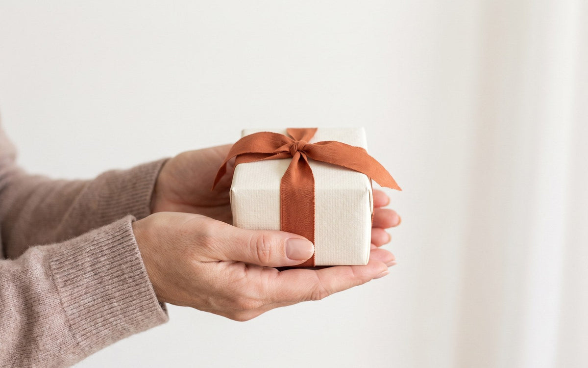 regalo per la mamma: due mani che porgono un pacchetto avorio chiuso con un nastro arancione