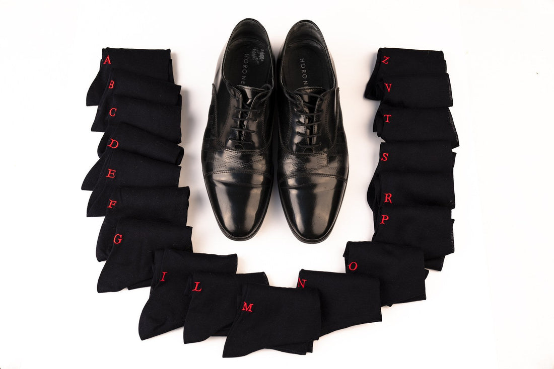 regalo per il nonno: calze nere con le iniziali ricamate in rosso, disposte intorno a un paio di scarpe stringate nere