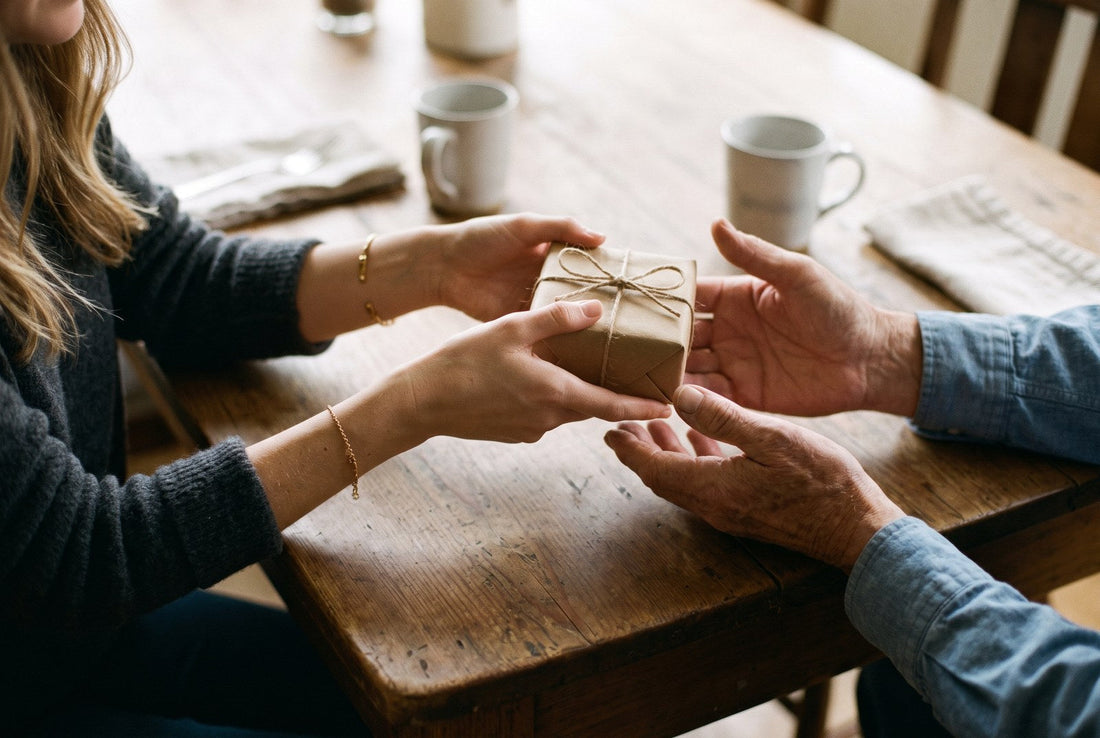 regalo per papà: una figlia consegna al padre un pacchetto in carta kraft con il fiocco di spago, su un tavolo di legno con due tazze